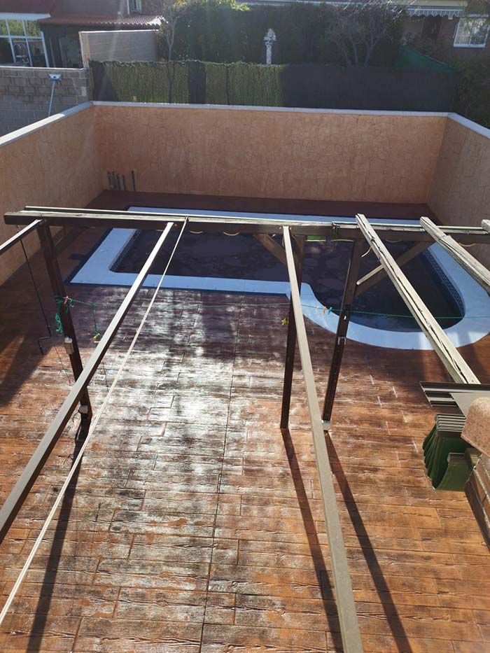 Patio con pequeña piscina y estructura metálica. Suelo imitación ladrillo marrón y paredes beige.