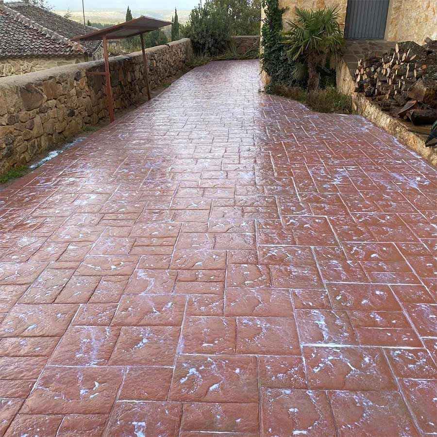 Pavimento rojo con diseño de ladrillo entre muros de piedra. Se ven manchas blancas.