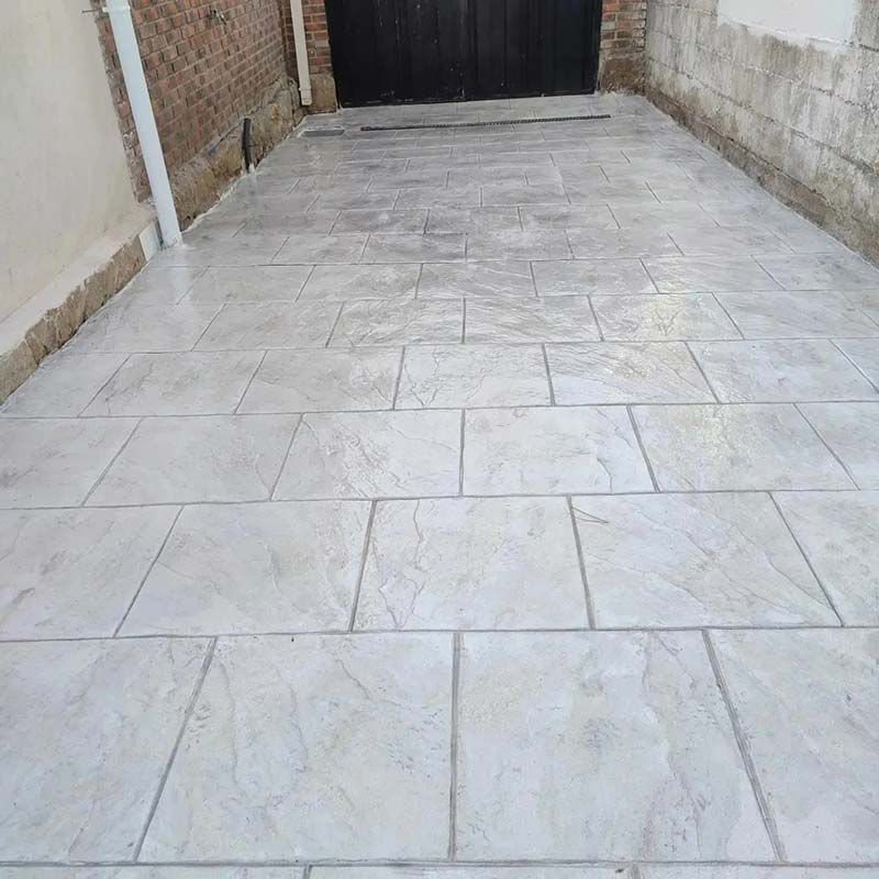 Entrada de hormigón estampado gris con paredes de ladrillo y piedra.