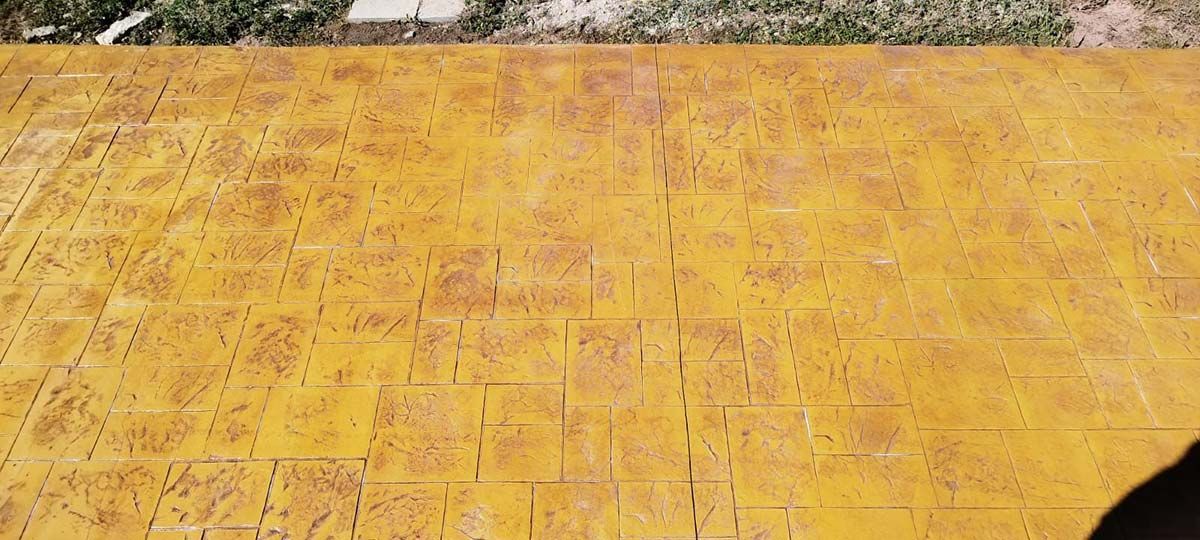 Vista aérea de un patio de ladrillo con textura amarilla con follaje verde arriba y sombra a la derecha.