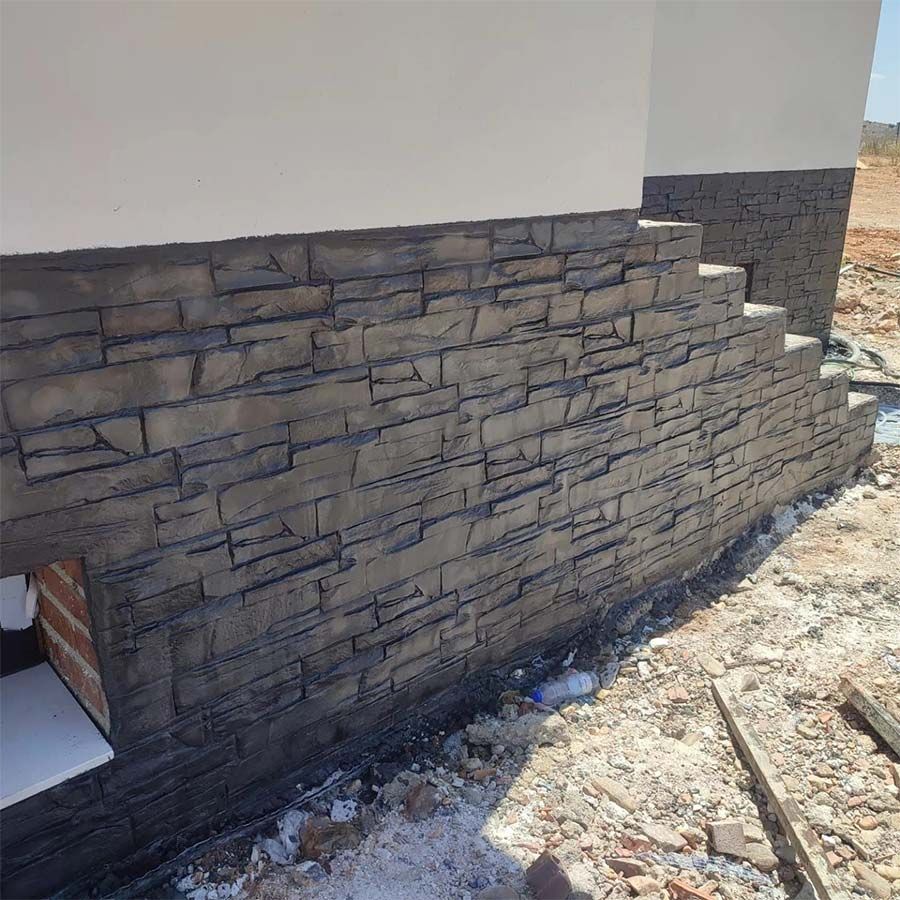 Revestimiento de chapa de piedra sobre cimientos de un edificio, color gris oscuro.