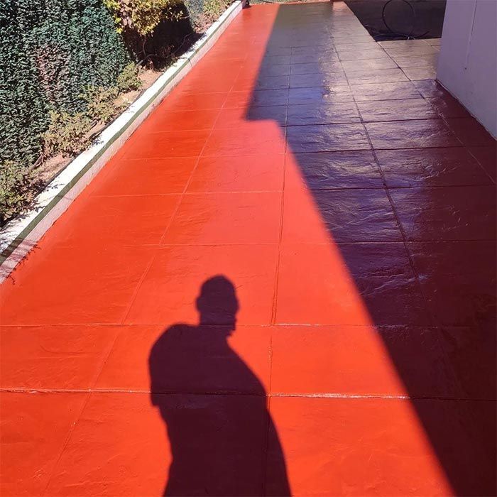 Una superficie de baldosas exteriores pintada de rojo con la sombra de una persona proyectada sobre ella.