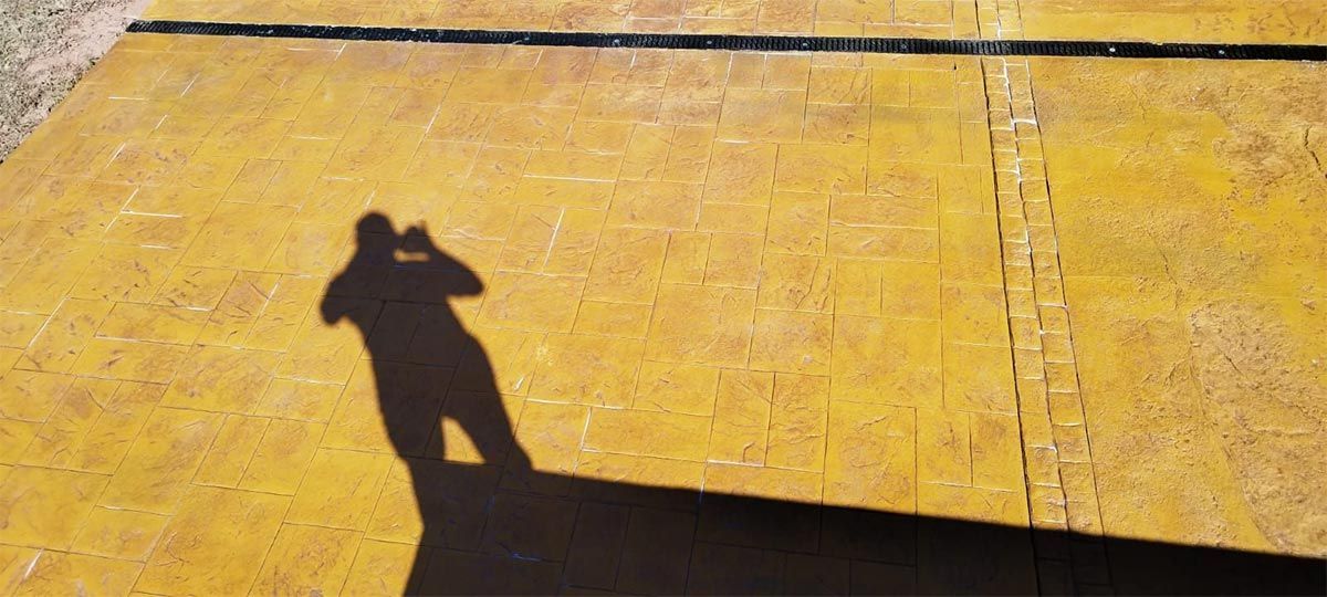 Sombra de una persona sosteniendo una cámara sobre una superficie amarilla con líneas.