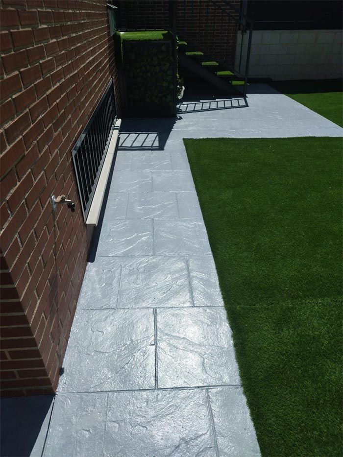 Pasarela de piedra gris al lado de un edificio de ladrillo y patio con césped verde.
