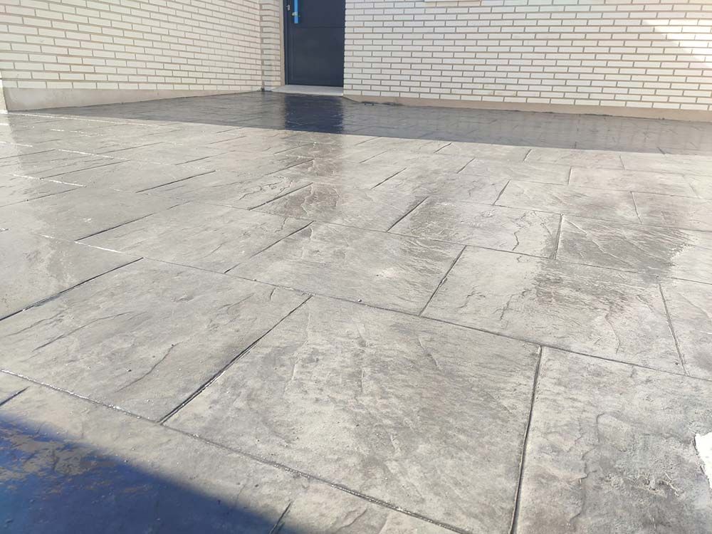 Patio de concreto estampado gris con pared de ladrillo y puerta negra.