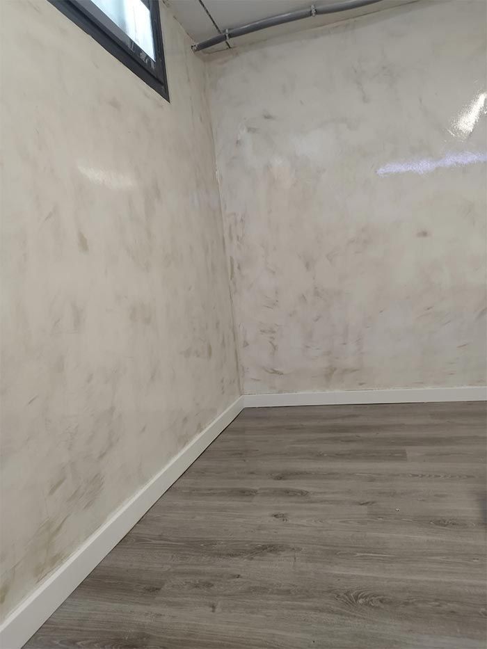 Habitación con paredes con acabado falso en crema y gris, zócalos blancos y piso con apariencia de madera.