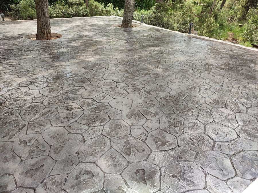 Patio de concreto estampado con diseño de piedra gris, dos árboles al fondo.