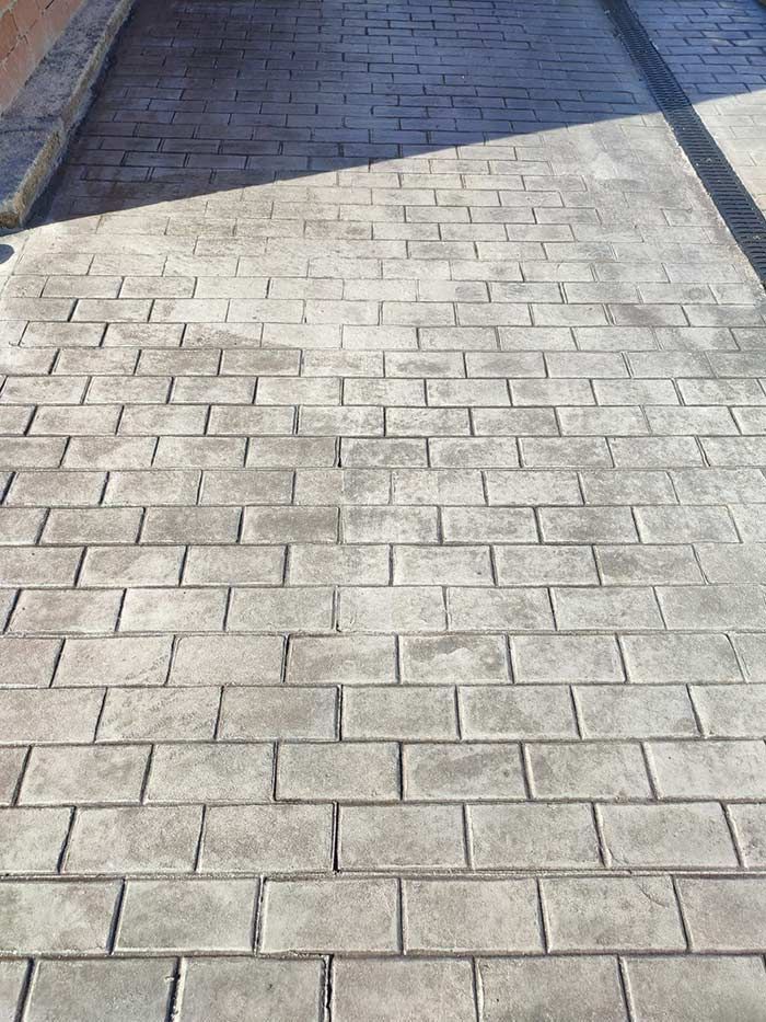 Entrada de hormigón estampado de color gris con diseño de ladrillo.