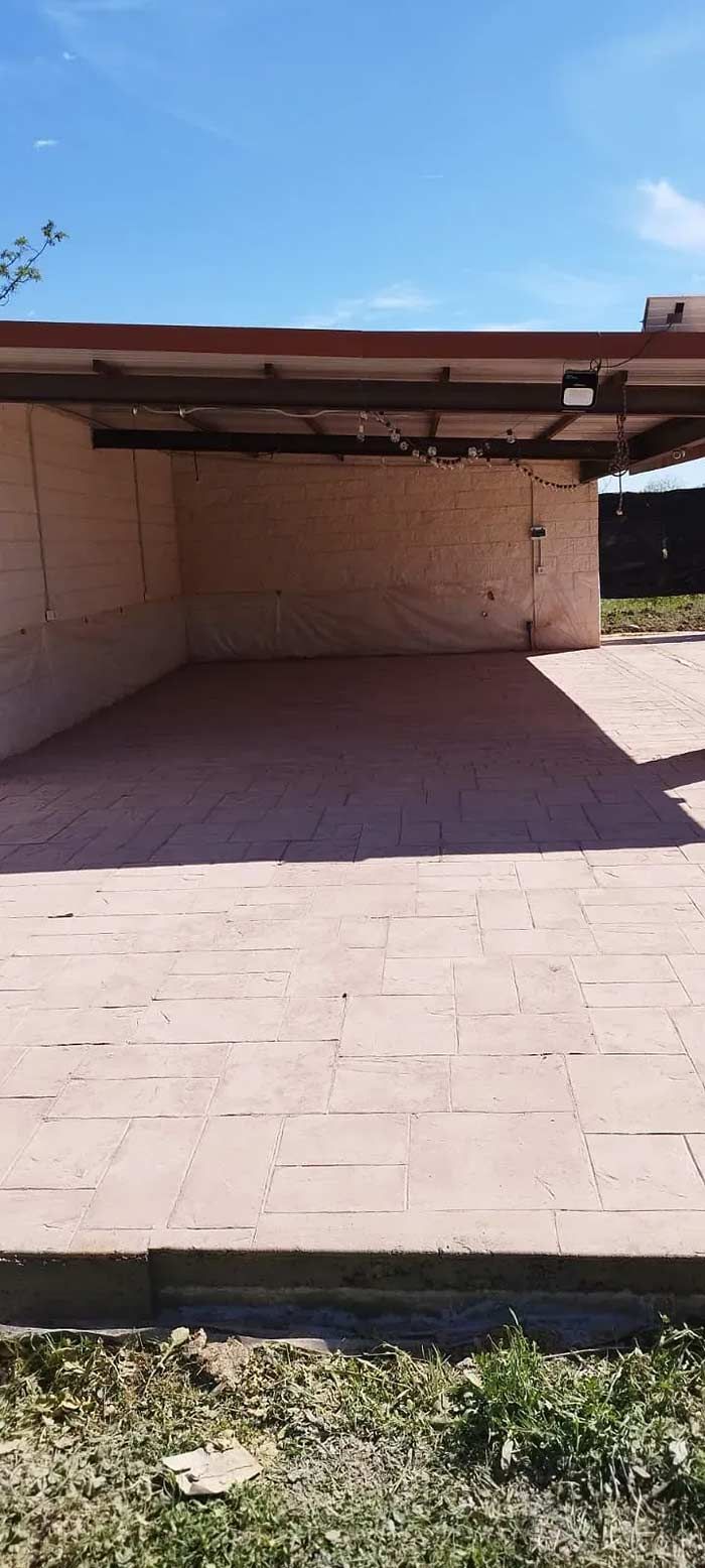 Una cochera vacía, abierta por un lado, con suelo de baldosas. Se ve el cielo azul.