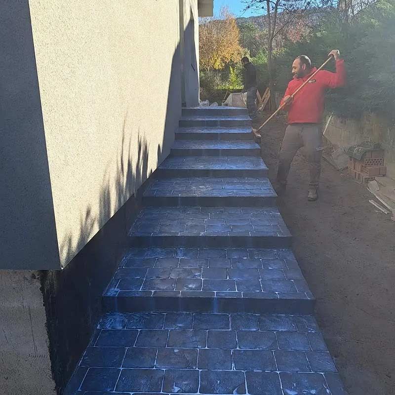 Escalones de piedra que suben junto a un edificio. Una persona está trabajando en los escalones.