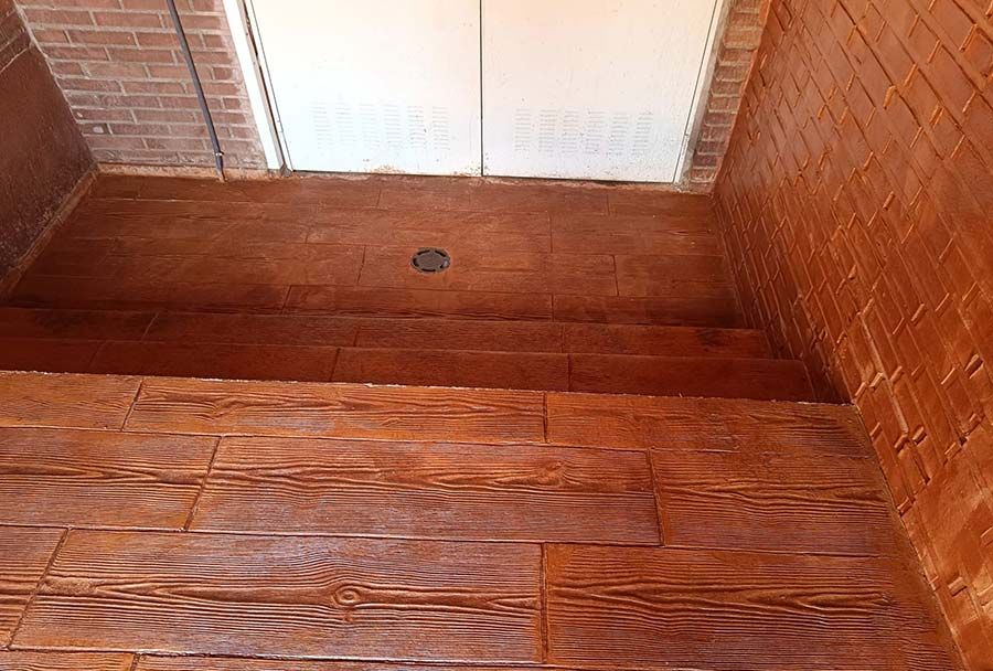 Ducha de hormigón marrón con textura imitación madera en suelo y paredes. Se ve un pequeño desagüe.