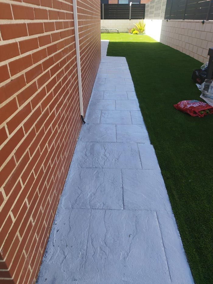 Pared de ladrillos al lado de una pasarela gris estampada que conduce a través de césped artificial verde.