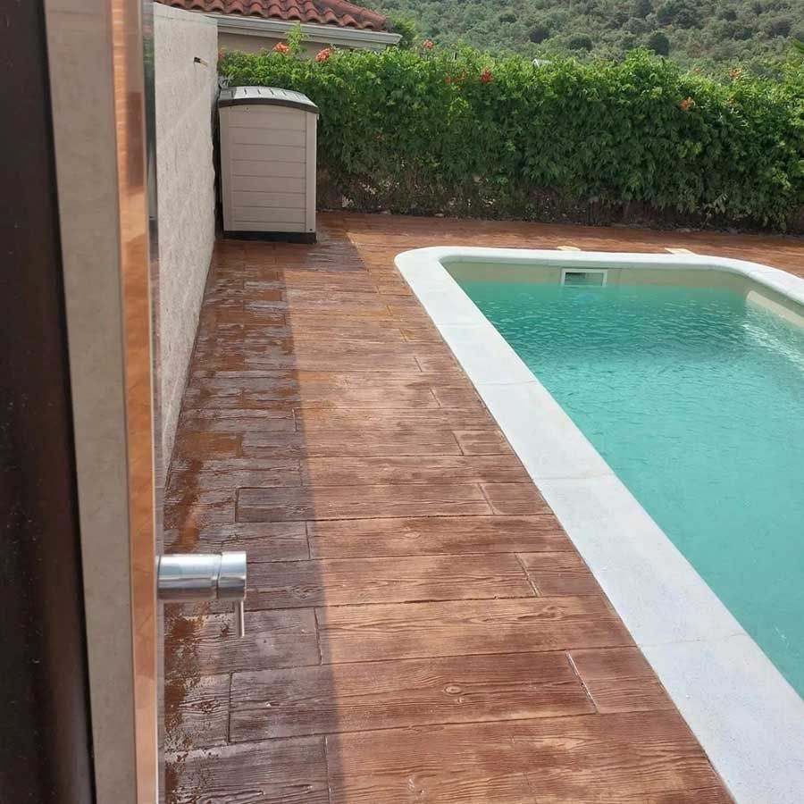 Zona de piscina con piscina rectangular, pavimento imitación madera y contenedor de almacenaje de color beige.