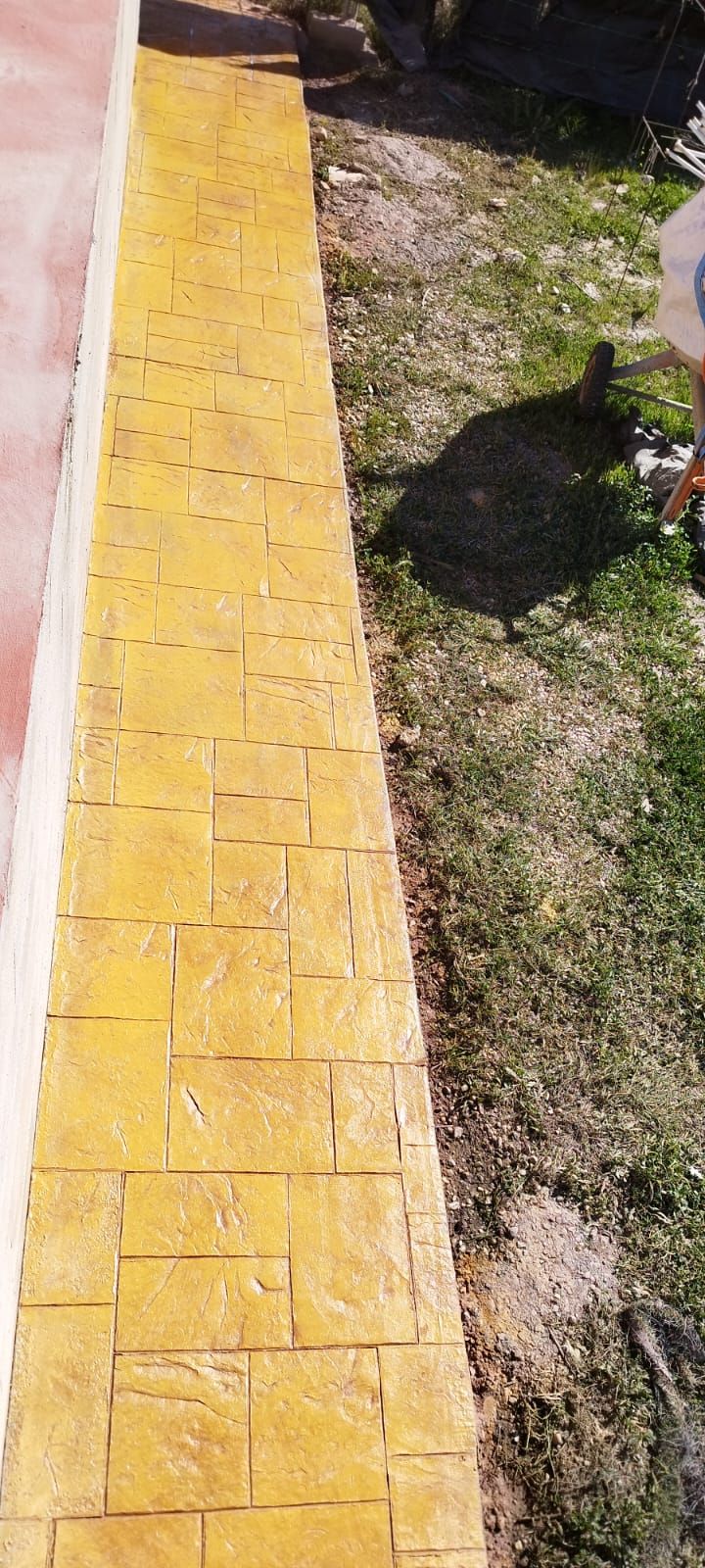 Se está construyendo una pasarela de ladrillos amarillos al lado de una zona verde.