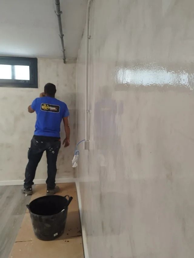 Un hombre con una camisa azul está pintando una pared en una habitación.