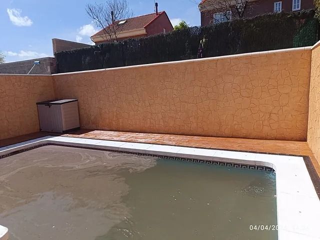 Una piscina está rodeada por un muro y una valla.