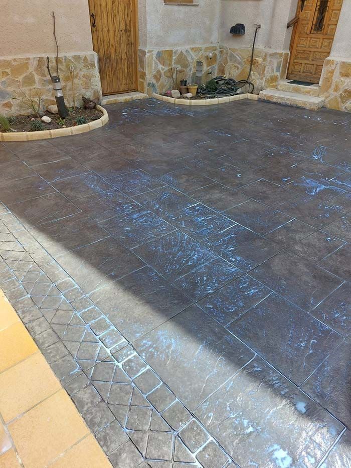 Patio de hormigón estampado de color oscuro, parches de color azul claro y borde de piedra cerca de las puertas.