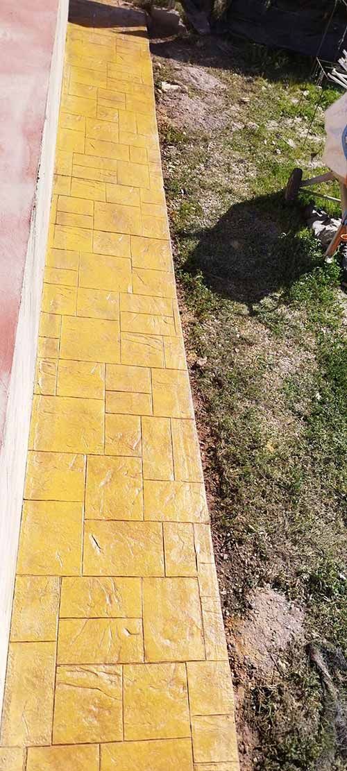 Camino de ladrillos amarillos al lado de una zona de césped, junto a una pared roja.