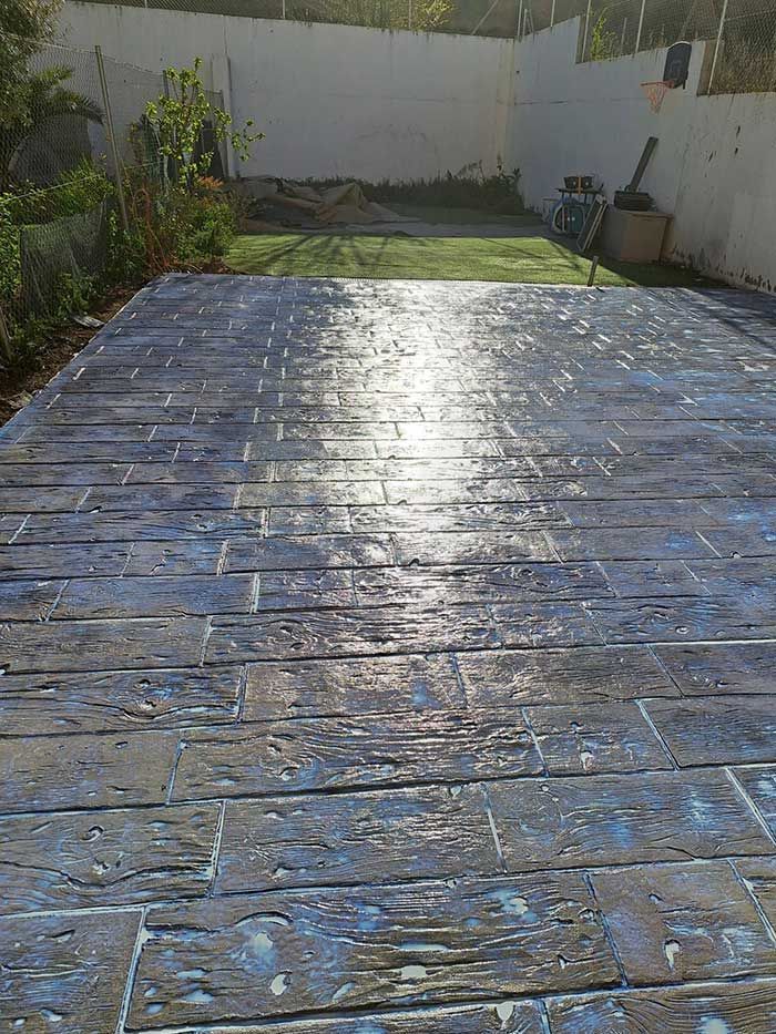 Patio de concreto estampado con textura de veta de madera, color gris azulado, en un entorno de patio trasero.