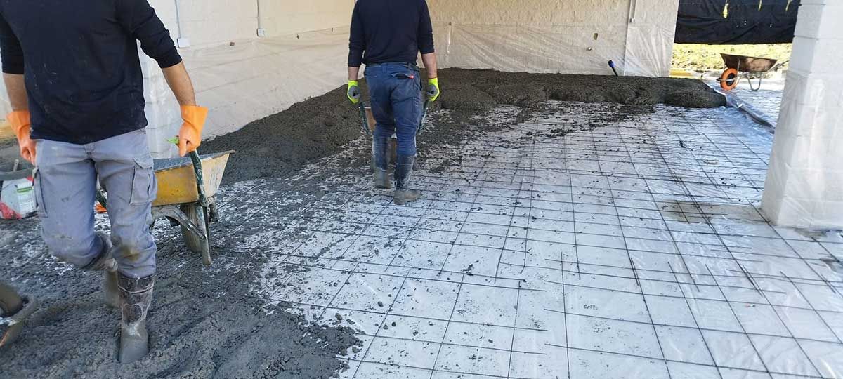 Trabajadores vierten hormigón sobre una superficie en forma de cuadrícula bajo una carpa blanca.