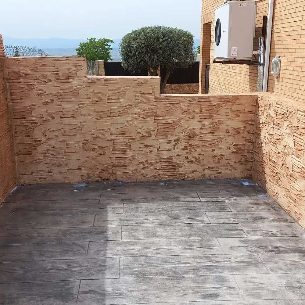 Patio con textura de piedra, suelo de hormigón impreso y pared de ladrillo, con vistas al paisaje. Se ve un aparato de aire acondicionado.