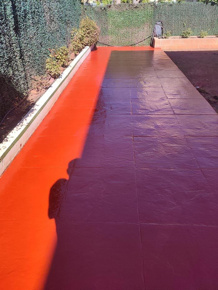 Camino de hormigón rojo con una sombra proyectada sobre él, al lado de un seto verde.