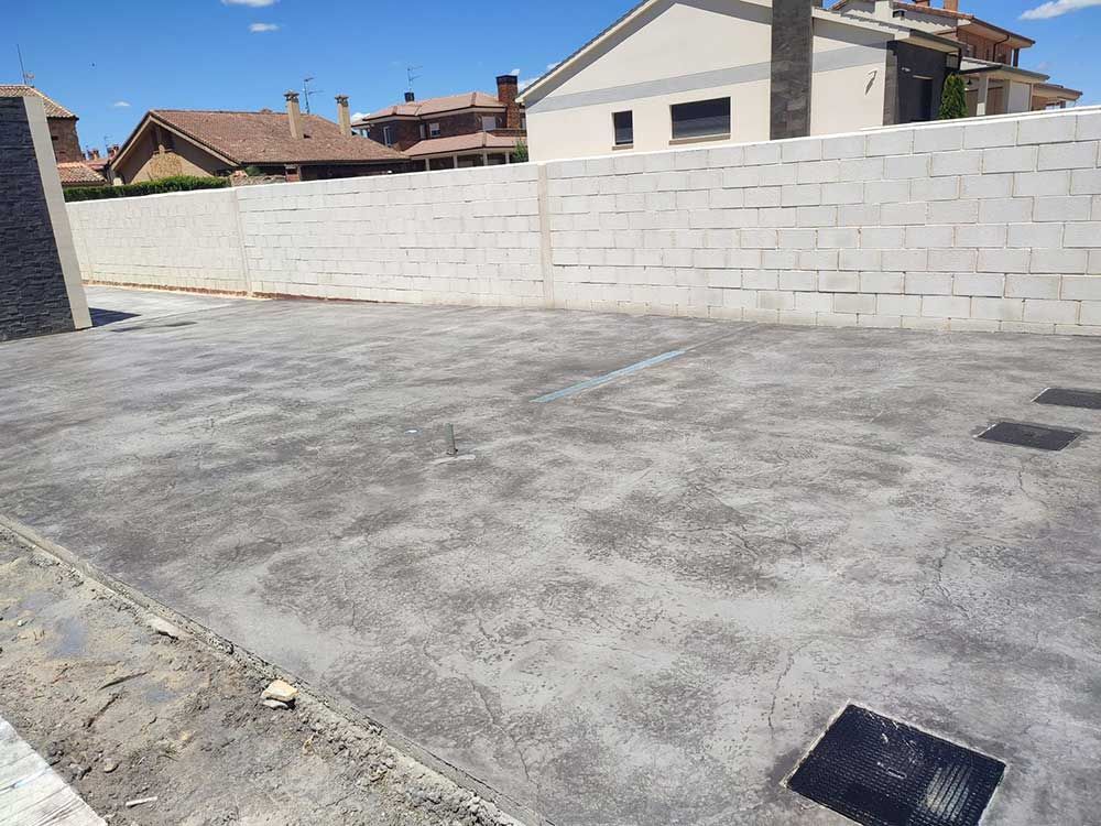 Camino de entrada de hormigón con una pared de ladrillo blanco y casas al fondo en un día soleado.
