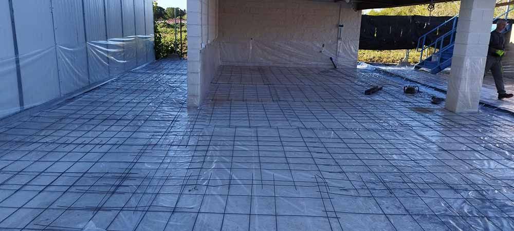 Obra con una malla de varillas corrugadas sobre una lona azul, lista para el vertido de hormigón. Una persona está de pie cerca.