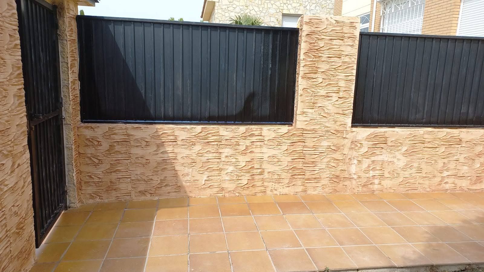 Un muro de ladrillos con una valla negra y un patio delante.