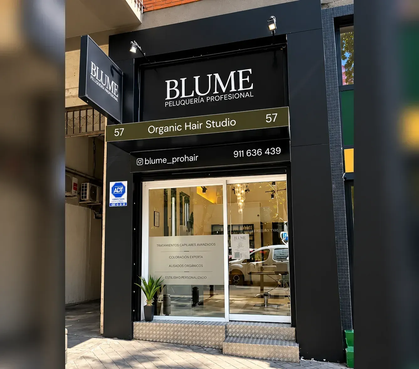 Fachada de BLUME Organic Hair Studio, con puerta de cristal y letrero negro en una calle de la ciudad