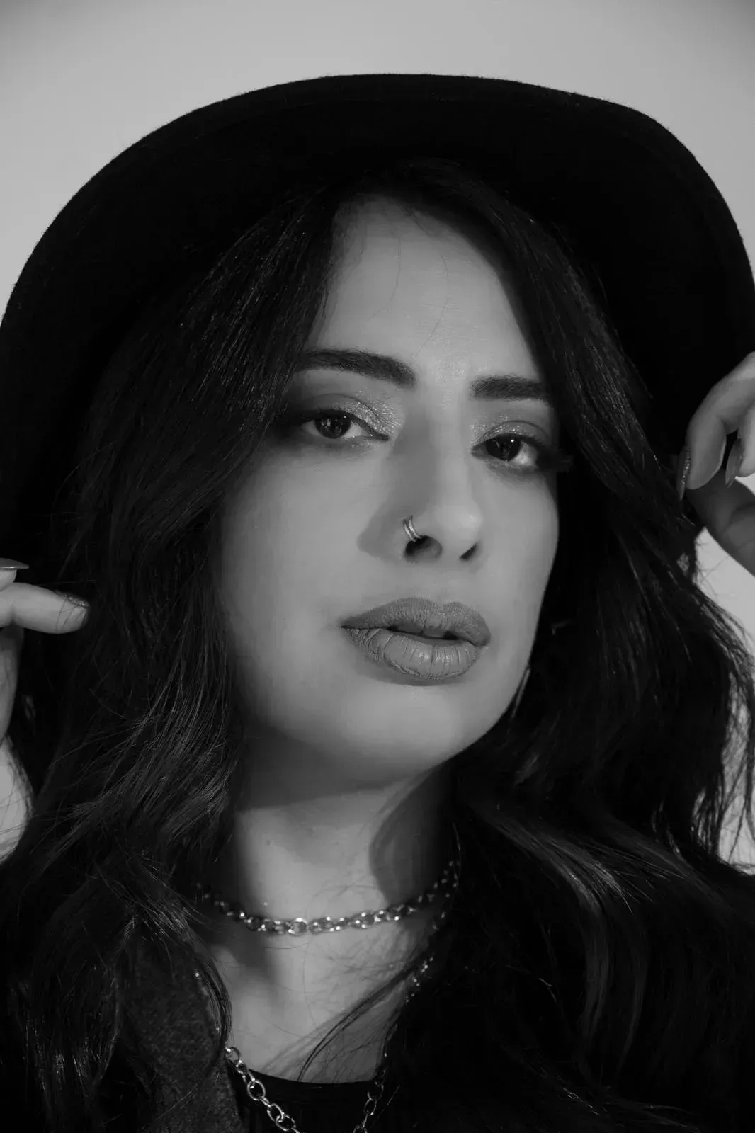 Retrato de una mujer con sombrero negro, mirando a la cámara sobre un fondo liso.