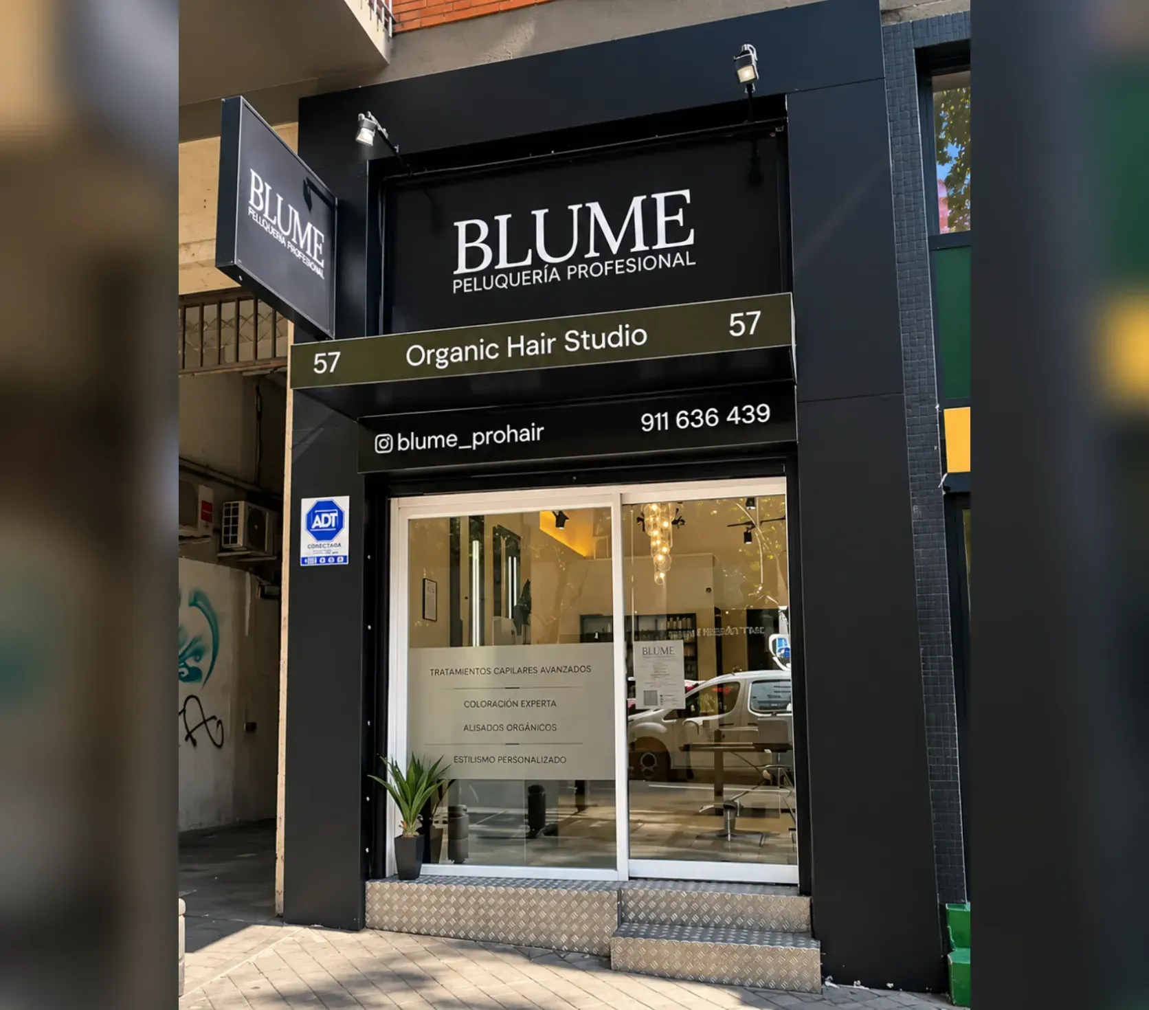 Fachada de BLUME Organic Hair Studio, con puerta de cristal y letrero negro en una calle de la ciudad
