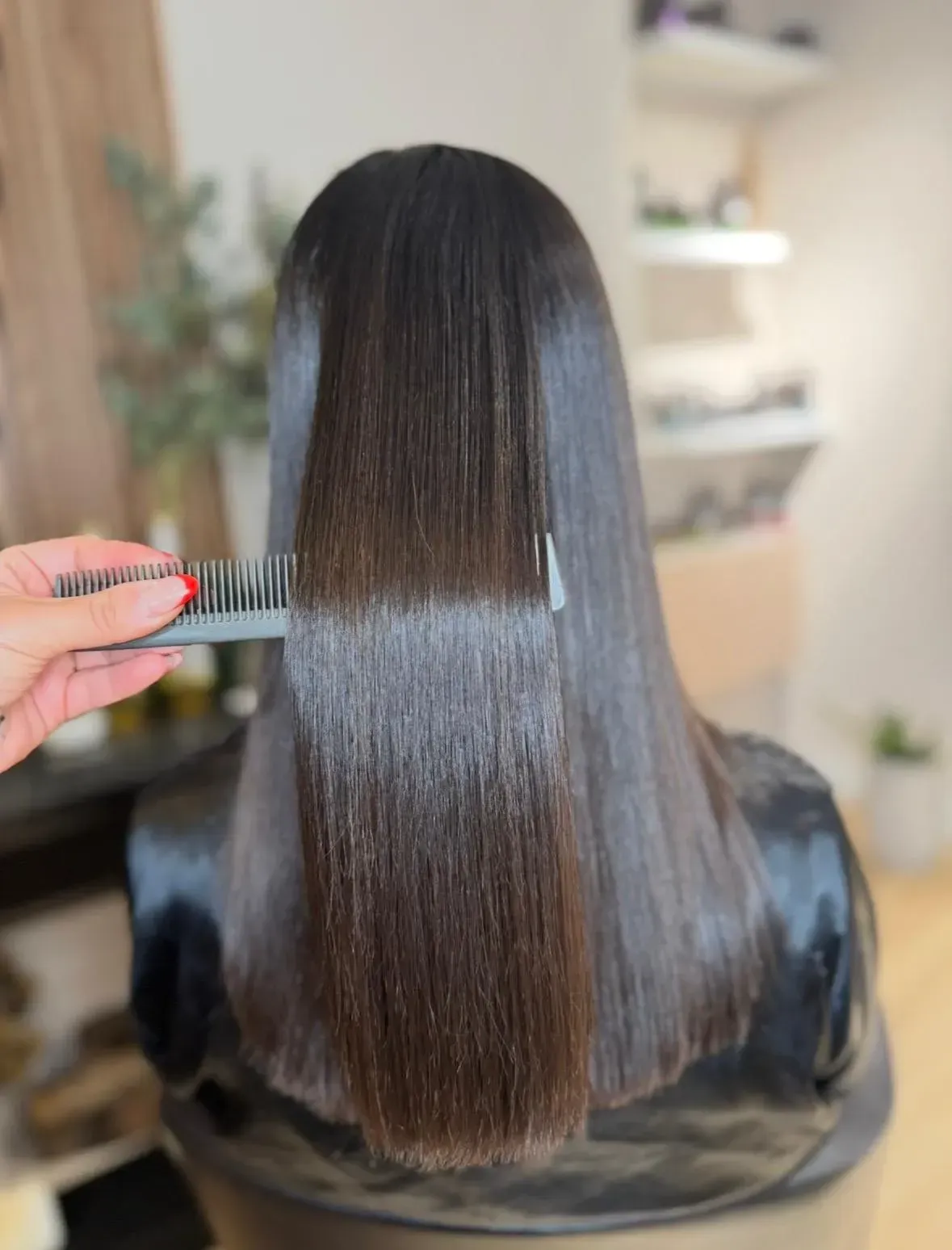 Peluquero peinando el cabello liso y brillante de color negro de una clienta sentada en un salón de belleza.
