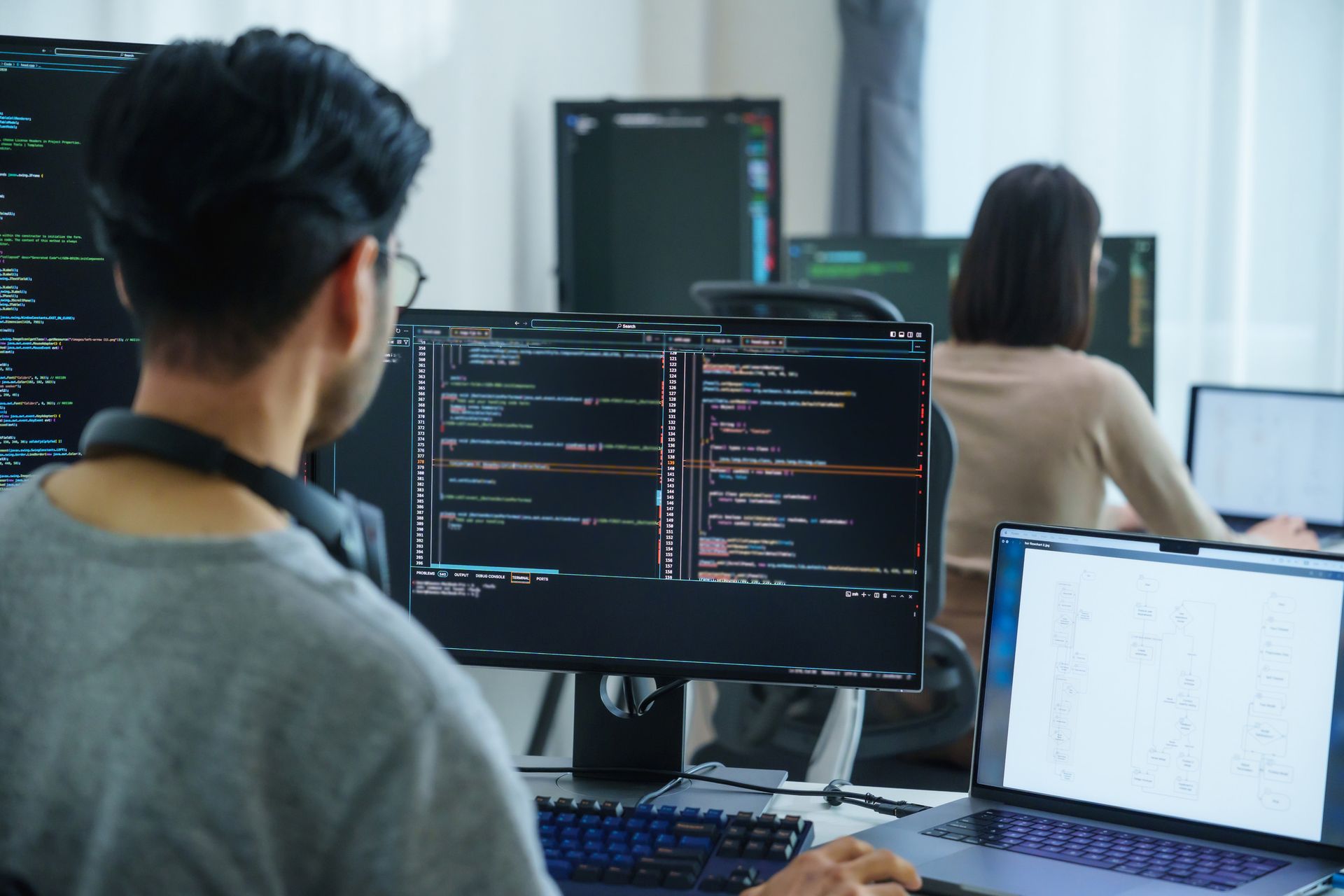 Hombre y mujer codificando frente a pantallas de computadora en una oficina moderna.