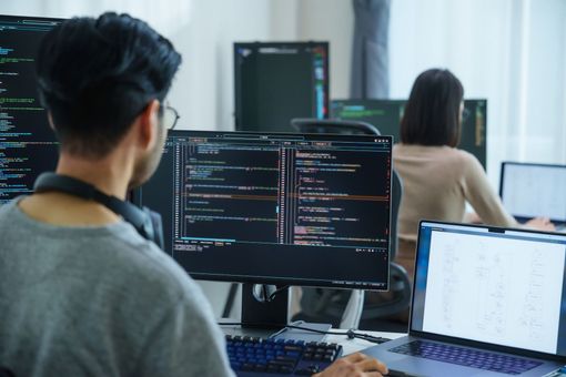 Hombre y mujer codificando frente a pantallas de computadora en una oficina moderna.