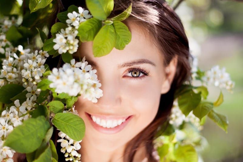 Frau lächelt hinter blühendem Busch hervor, Ingrid Mack partner for you