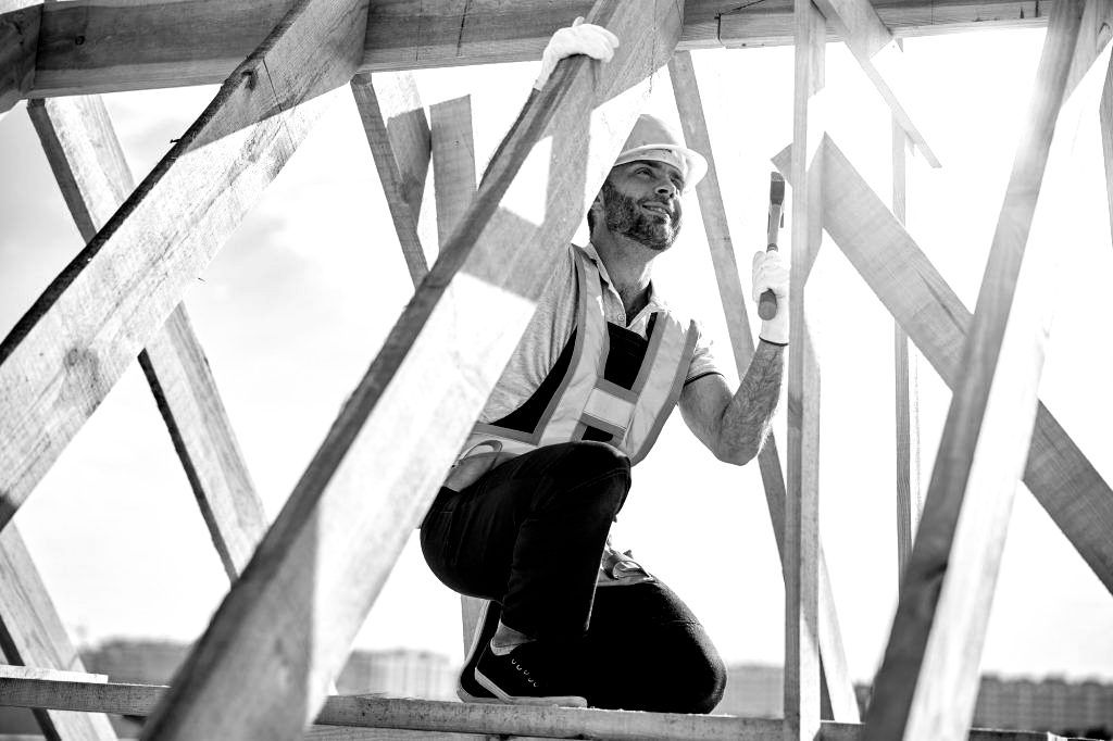 Une photo en noir et blanc d'un ouvrier du bâtiment agenouillé sur une structure en bois.