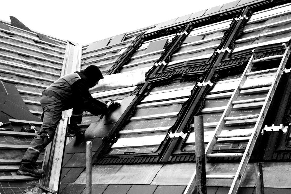 Un homme travaille sur le toit d'un bâtiment avec une échelle.