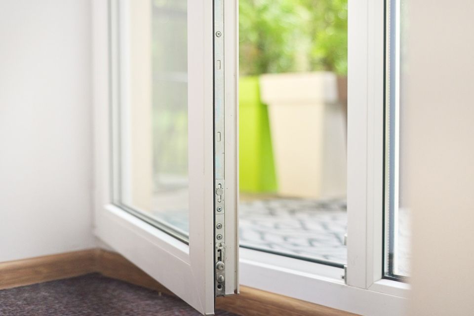 Fenêtre blanche ouverte donnant sur la verdure environnante. La pièce est dotée de plinthes brunes.