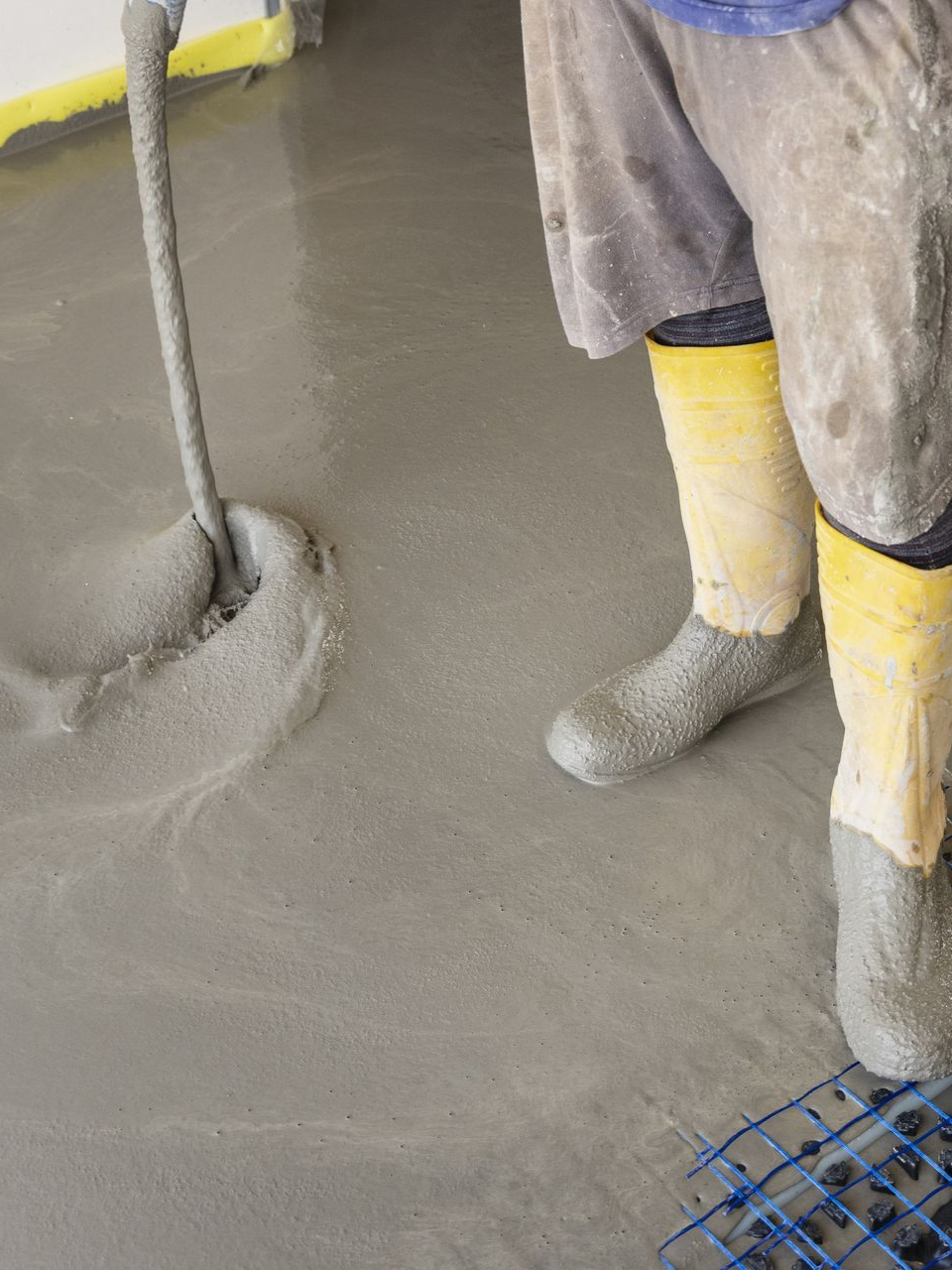 Un homme avec des bottes jaunes versant du béton liquide