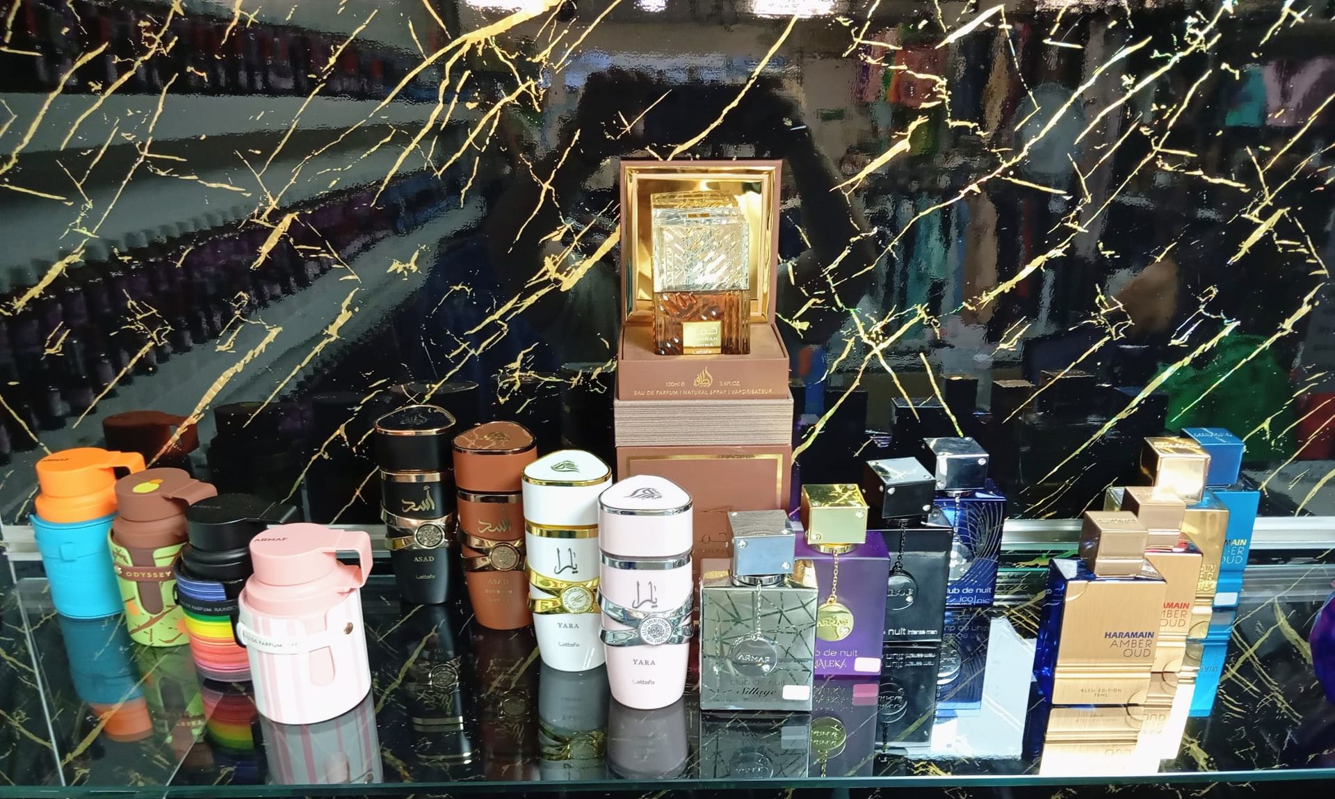 Frascos de perfume sobre una superficie negra delante de un espejo con vetas doradas.