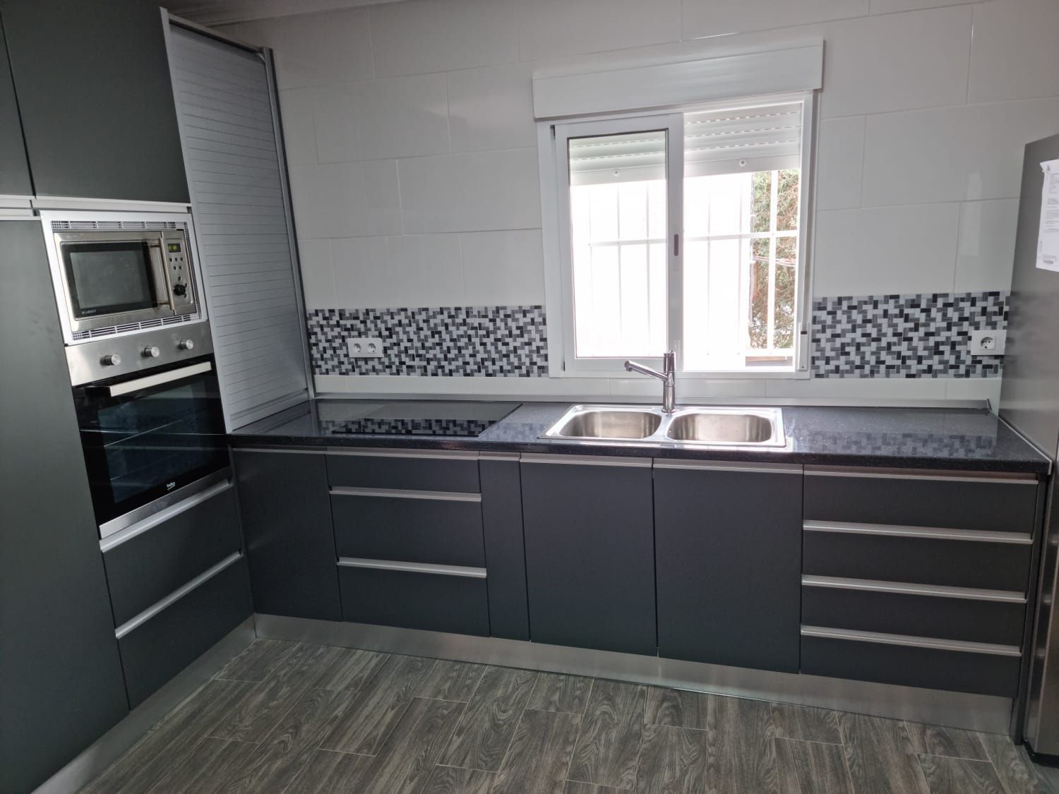 Una cocina con gabinetes grises, electrodomésticos de acero inoxidable, un fregadero y una ventana.