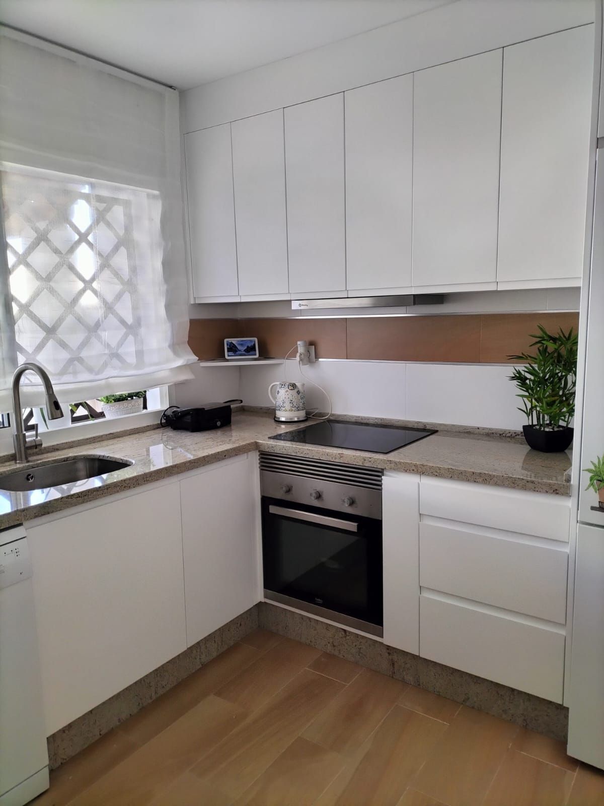 Una cocina con gabinetes blancos, una estufa, un fregadero y una ventana.