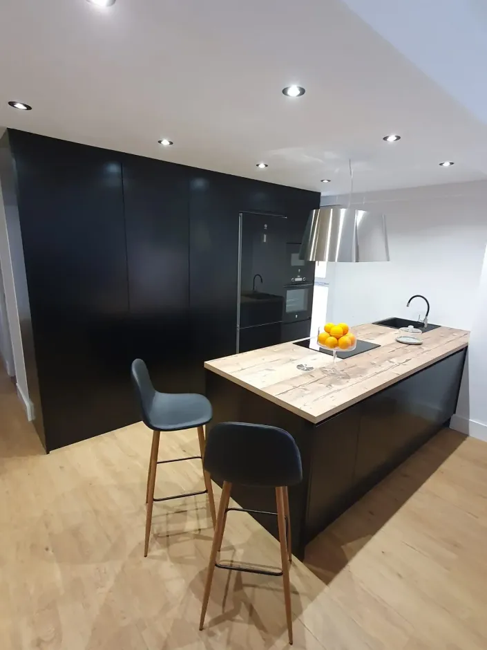 Una cocina con gabinetes negros y una encimera de madera.