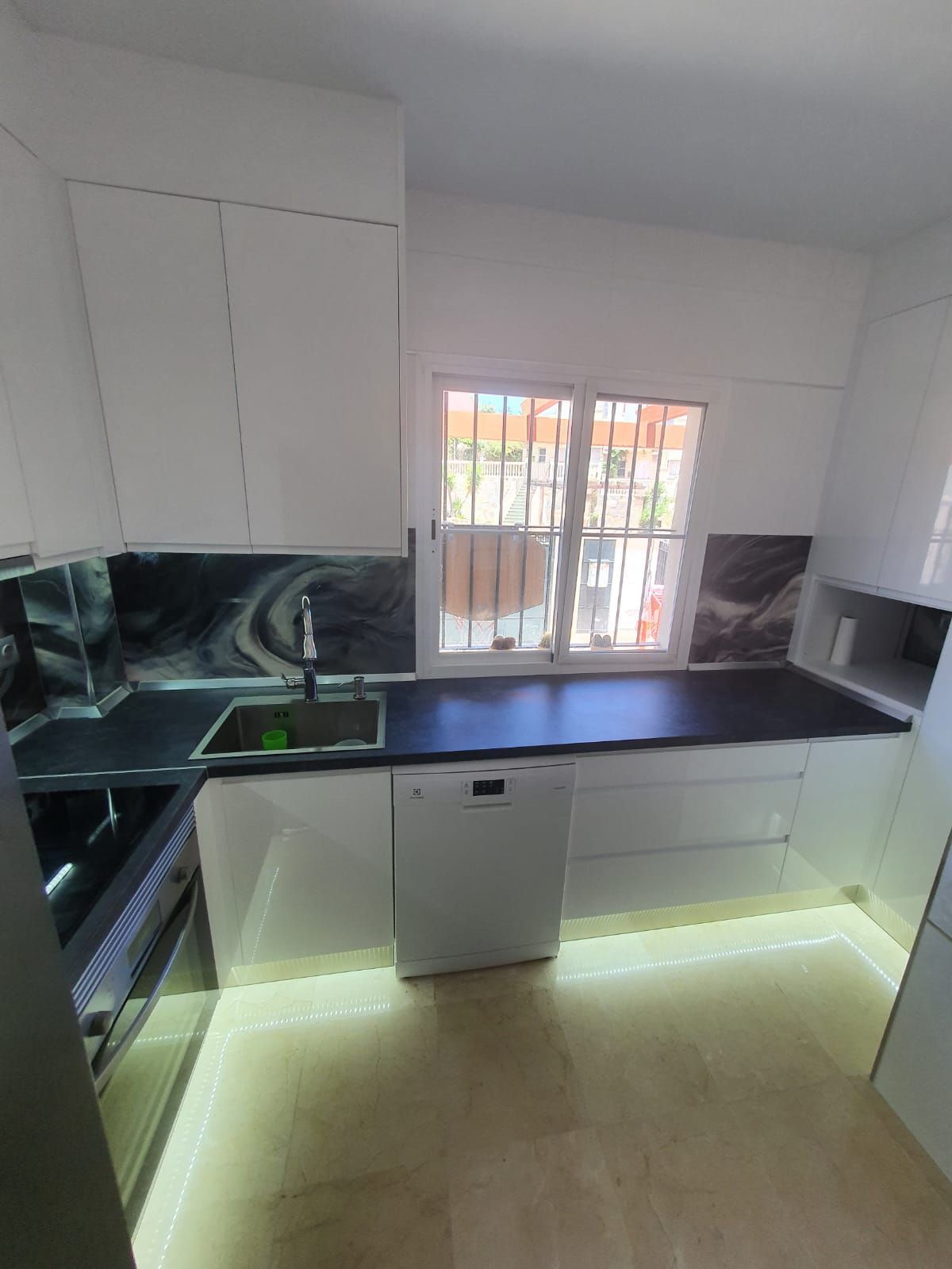 Una cocina con muebles blancos, un fregadero, un lavavajillas y una ventana.