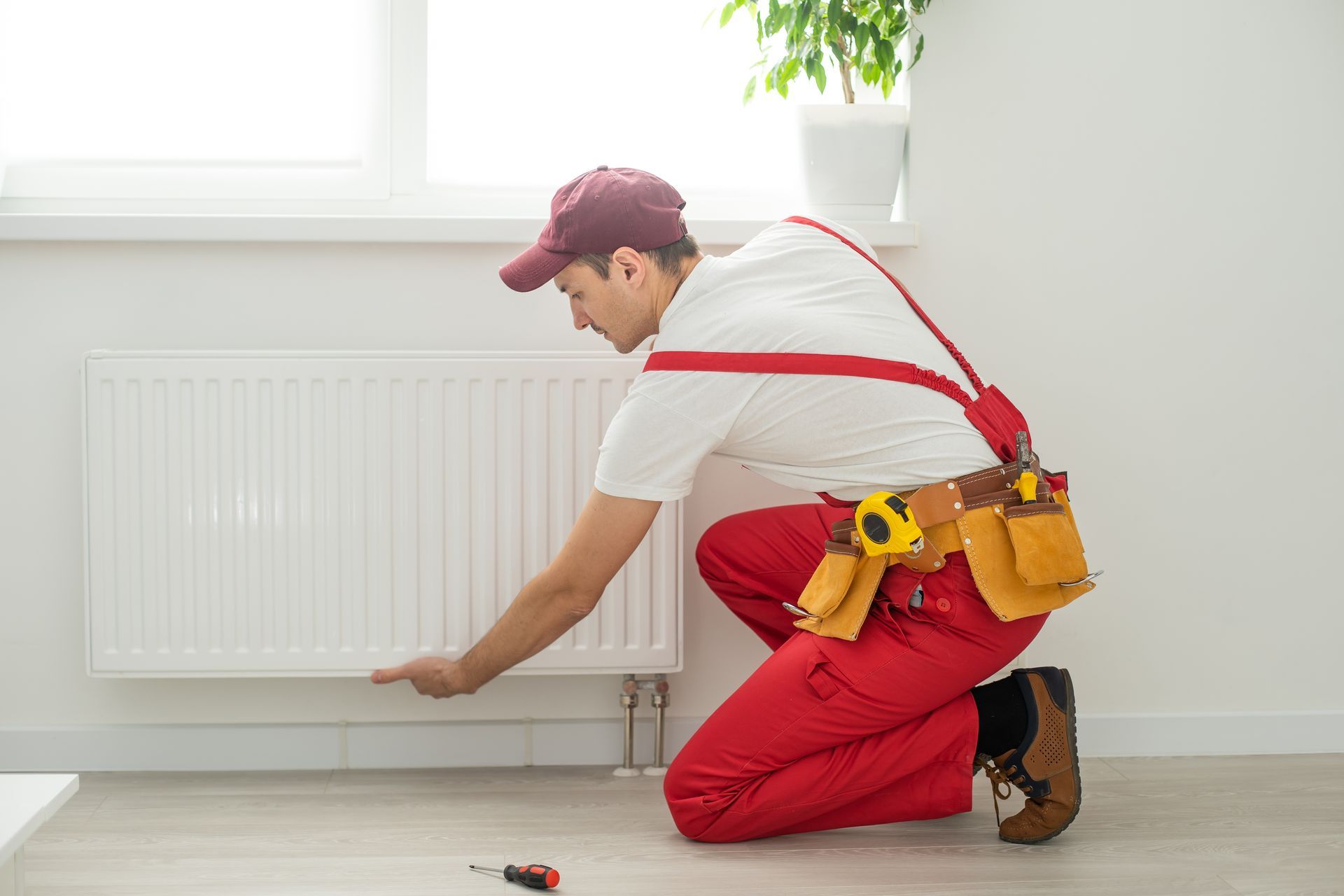 Un uomo è inginocchiato per riparare un termosifone in una stanza.