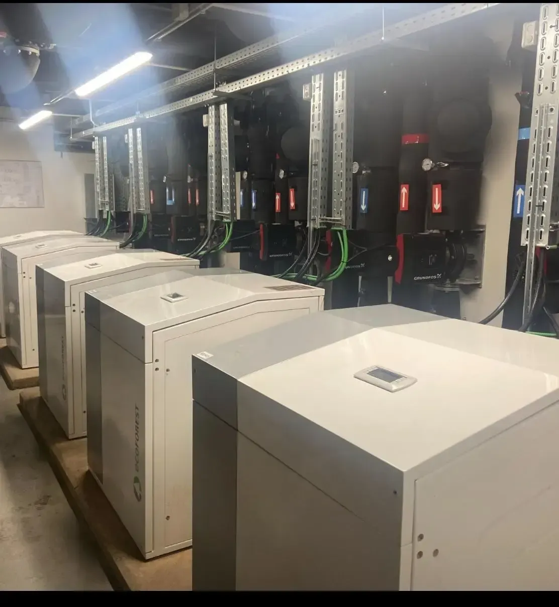 Unidades de almacenamiento de baterías alineadas en una sala industrial, con equipos eléctricos en la pared