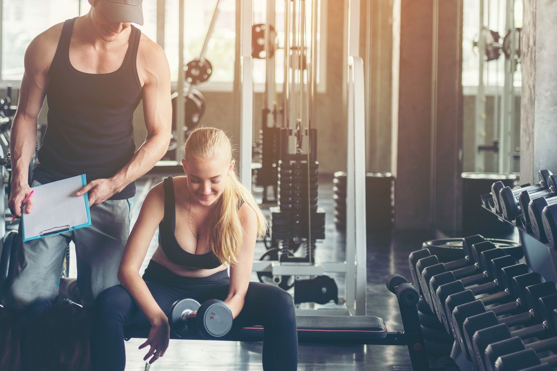 Un hombre está ayudando a una mujer a levantar una mancuerna en un gimnasio.