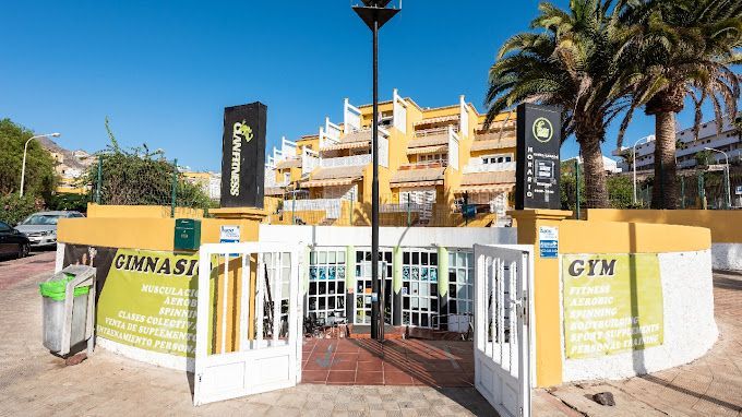 Un gimnasio está ubicado frente a un edificio con palmeras.