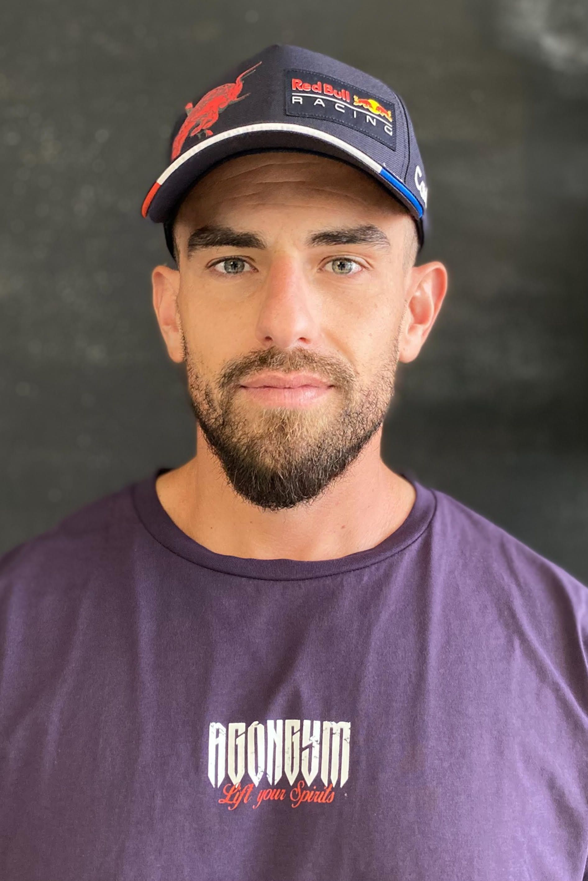 Un hombre con barba que lleva un sombrero de toro rojo y una camisa morada.